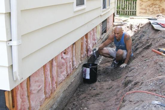 The architect specified a pressure-treated pony wall for resolving a grade problem along the side of the house. The crew exposed the foundation and framing, applied a coat of cold asphalt to the rim-joist area.