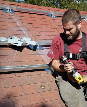 The modules will be grouped in two separate “strings,” so only two roof penetrations are required for the entire 38-module array. A waterproof plastic junction box at each penetration is carefully sealed to the shingles with silicone to prevent leaks.