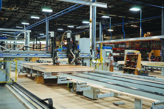 The CNC bridge gantry is equipped with nailers and a router. It travels over the wall on the table, fastening the sheathing to the framing and trimming it to the final panel size as well as cutting out the sheathing for any door and window openings.