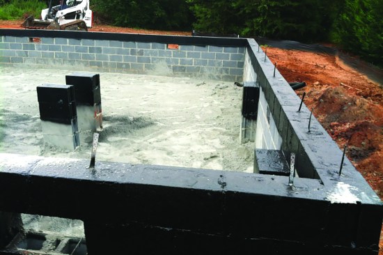 During construction, the waterproofing crew applies a temporary ground cover and applies waterproofing to the wall top and the tops of the interior masonry piers.