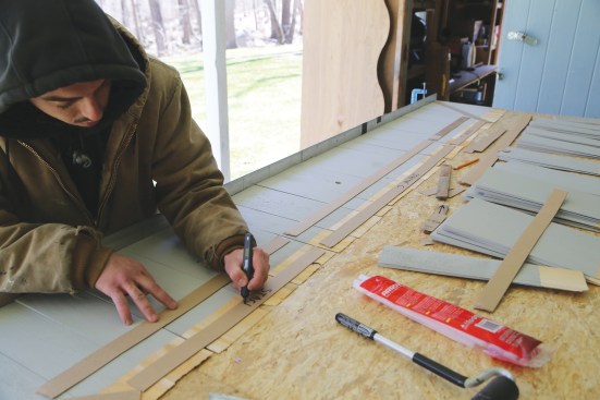 A worker labels the three collated shingle strips making up the course. He gives each one a course number and a location: center, left, or right.
