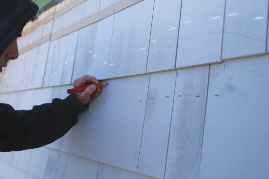 After the first of the two interceding courses is installed, the base course shingle strips have to be removed so that the second straight-shingle course can be installed. A worker needs to make marks that show where the shingle joints of the base course land.