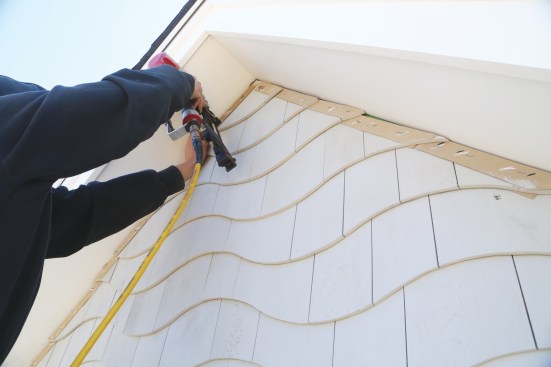 He installs the rest of the shingle strips course by course from the centerline out, aligning them with the faint pencil exposure line along the bottom.