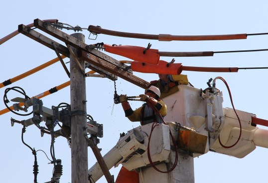 Utility workers maintain a power pole in Boston, Mass., in 2014. Power companies say homeowners with rooftop solar panels aren’t paying their full share of the operating cost of the power transmission grid, even though they often draw power from the system.
