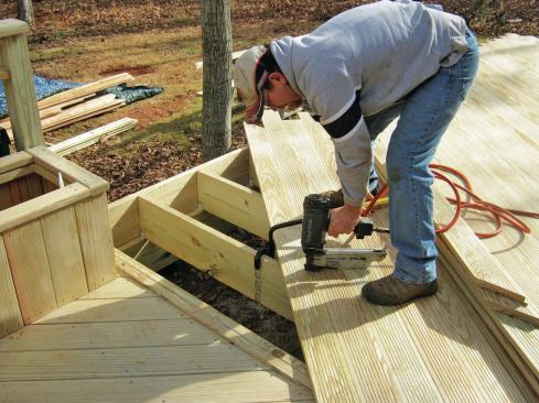 A worker fastens the author’s custom-milled shiplap porch flooring to the framing with 2 1/2-inch-long stainless steel staples. This area will later be enclosed with a screened porch, so the joints between boards need to be tight to keep insects out. 